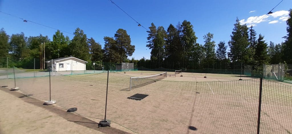 Kuvassa kaksi tenniskenttää ja vaaleankeltainen rakennus.